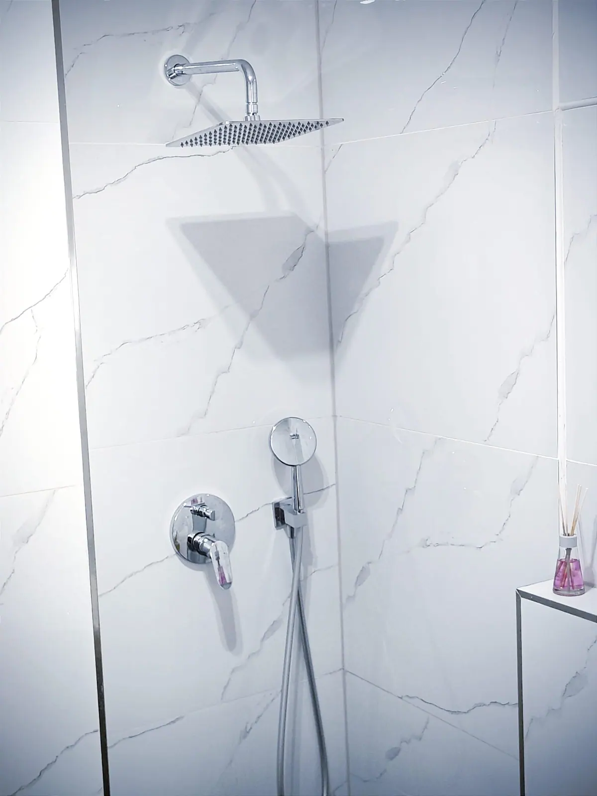 Regendusche in weißer Marmoroptik mit Glastrennwand und Duftstäbchen