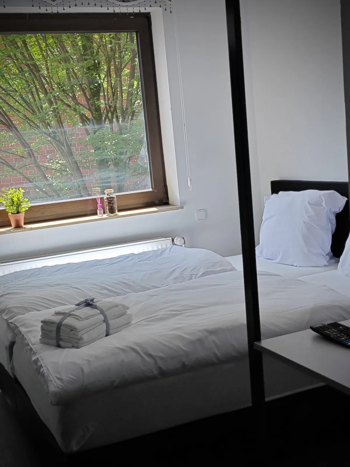 Zweibettzimmer mit Fernbedienung auf der Ablage und Fenster zum begrünten Innenhof